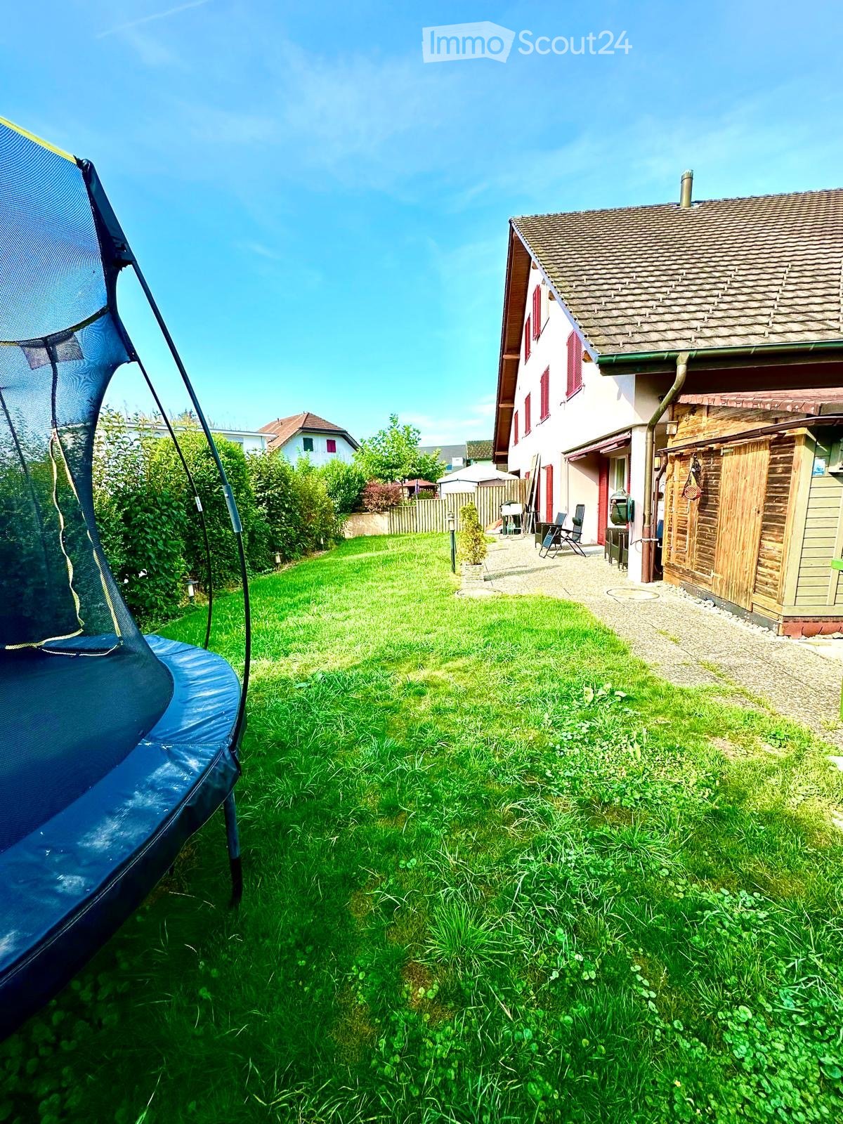 large green lawn, blue trampoline, well-maintained hedges, outdoor seating, small garden house