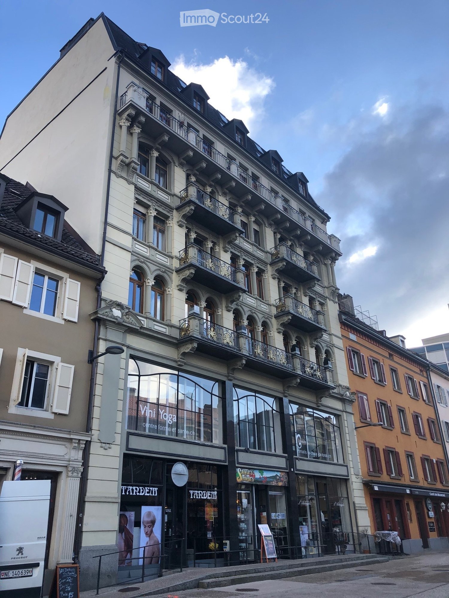 Elegant multistory building with several balconies and ornate designs, commercial storefronts on the ground floor.