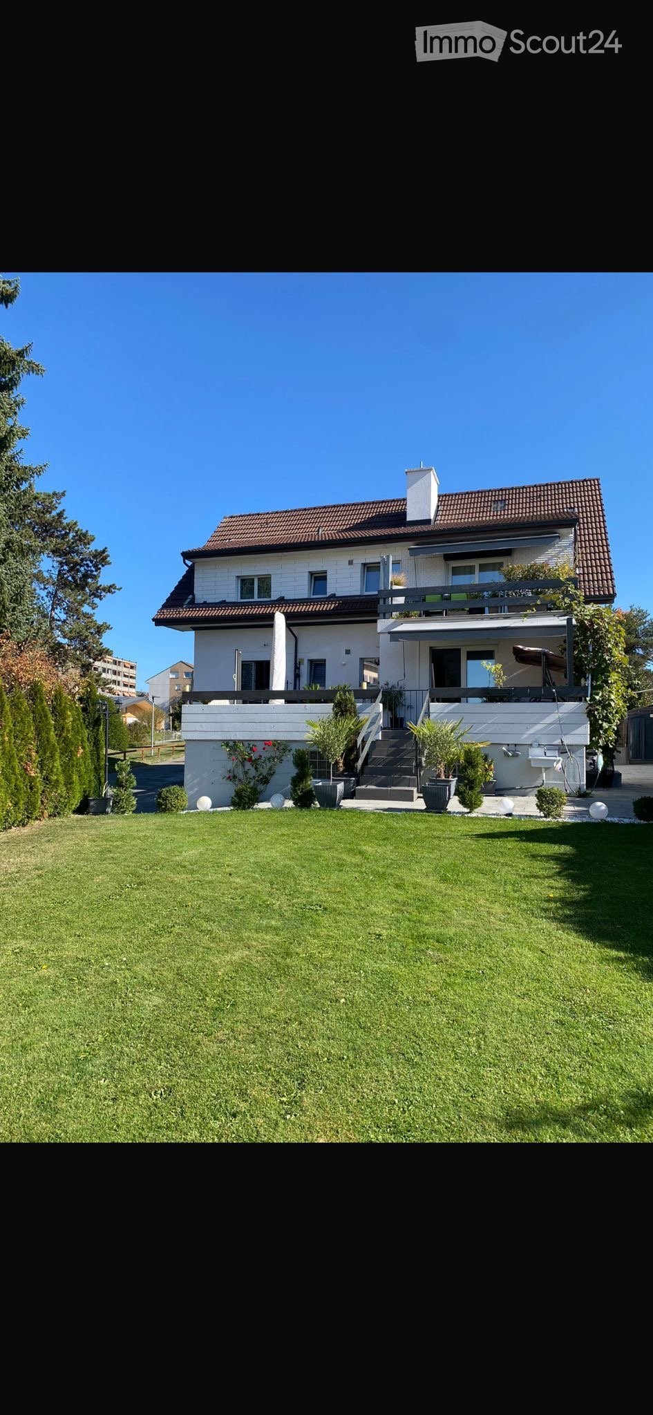 Two-story house, white exterior, brown roof, windows, balcony on second floor, stairs, garden, plants