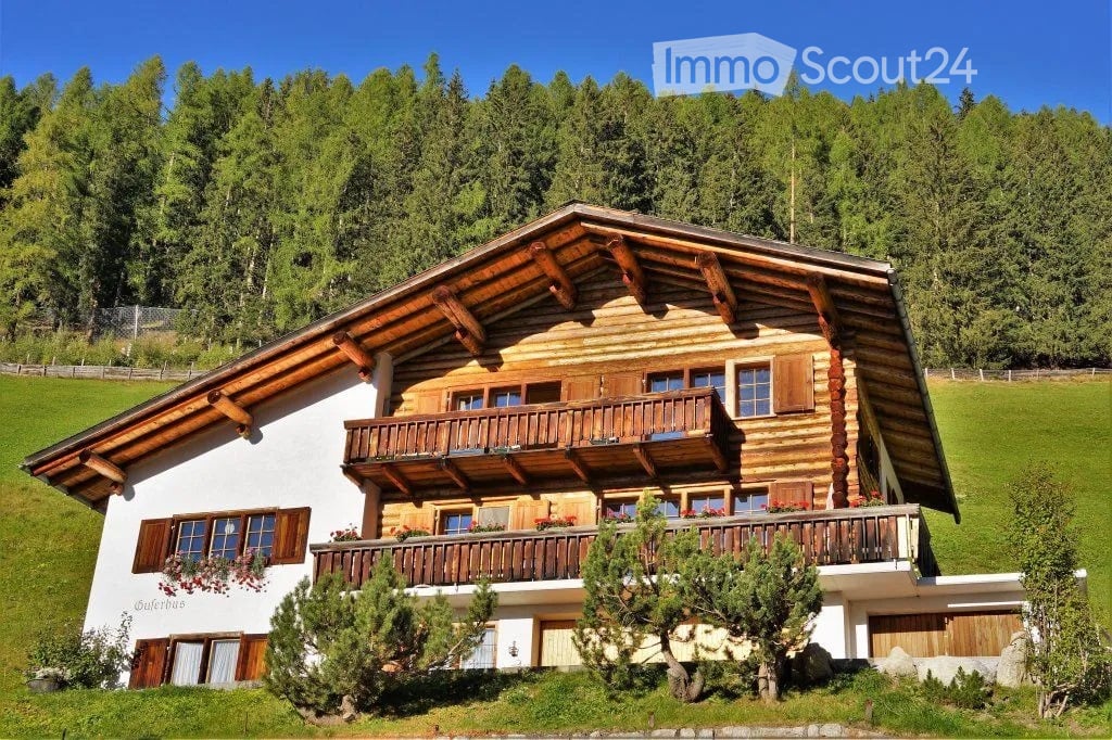 Mountain chalet with wooden balconies, surrounded by greenery and mountains