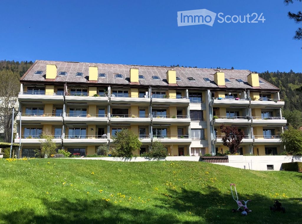 multi-story apartment building with balconies, yellow exterior, situated on a hill with lush greenery