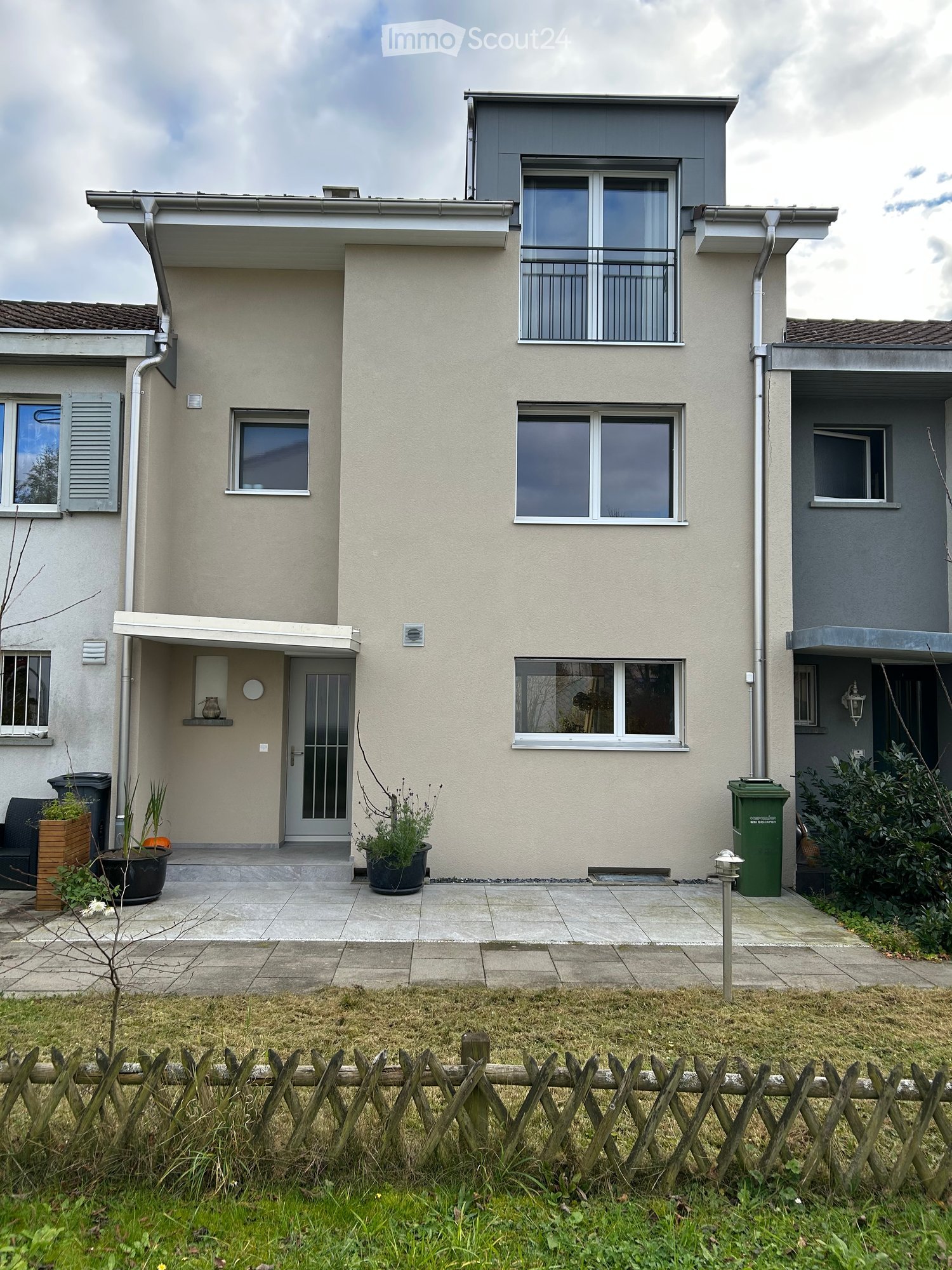 Three story house, beige, gray trim, balcony on second floor, small garden in front