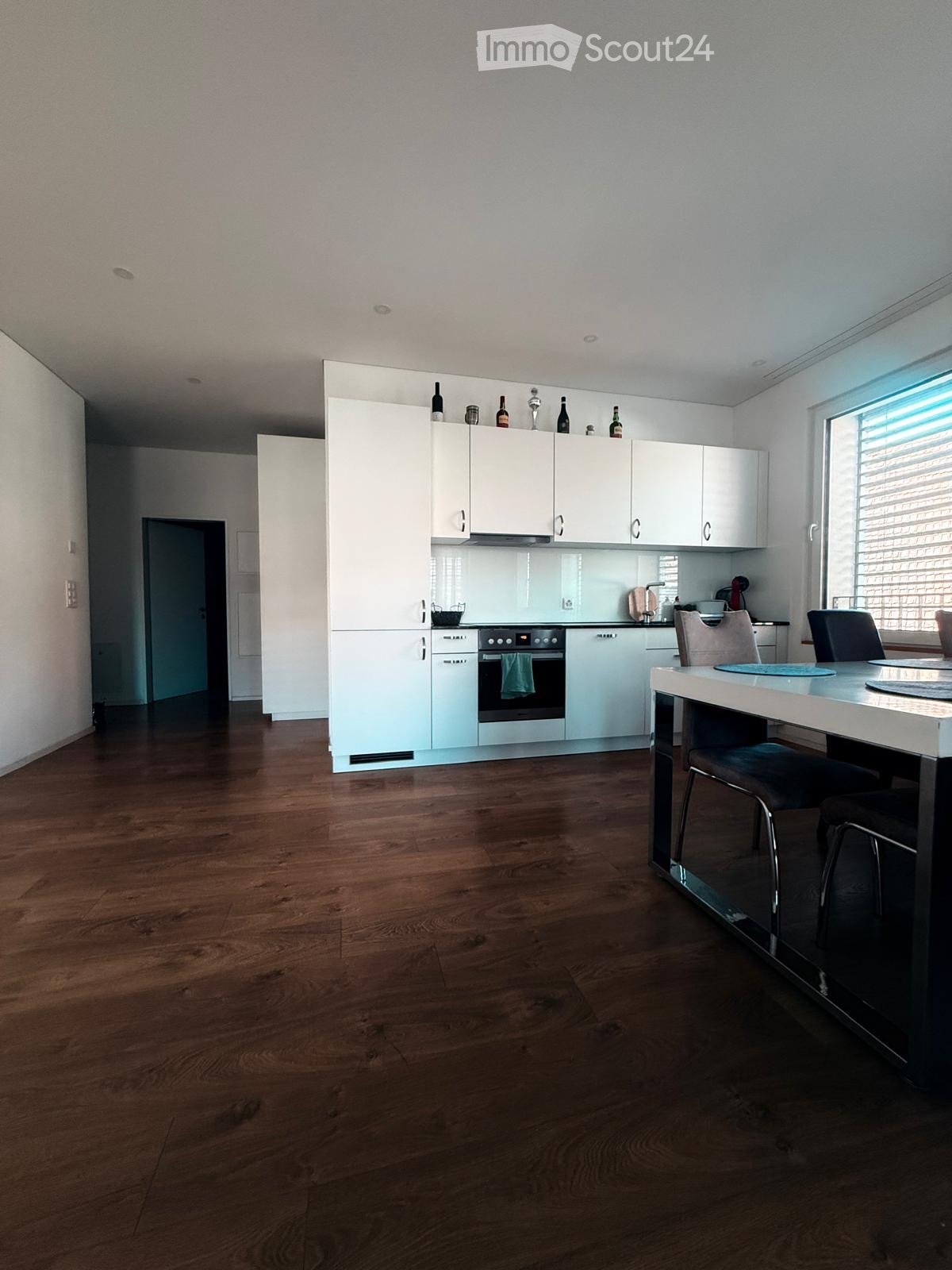 Kitchen with a modern design, a dining table with chairs, white cabinets, and built-in appliances, wooden floor, large window