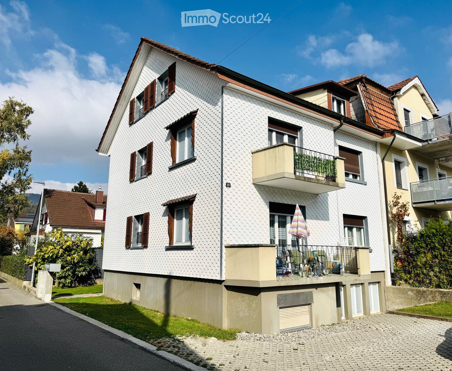 3 story house, white facade, brown roof, brown windows with shutters, balcony with outdoor seating, plants