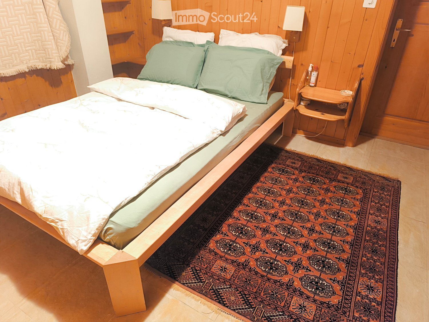 a bed with two pillows, carpet on the floor, wooden shelf on the wall