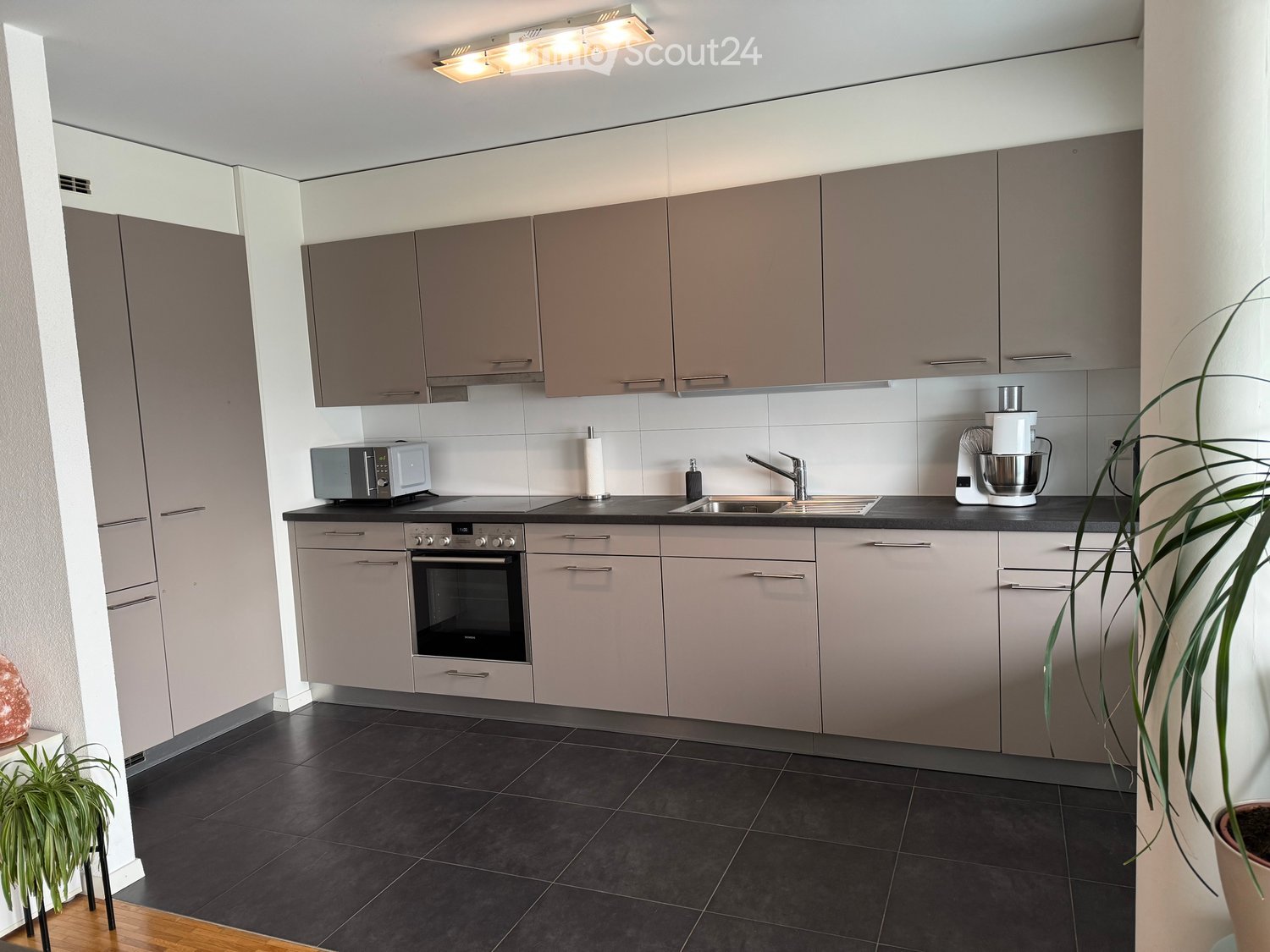 modern kitchen with wooden floor, built-in appliances, including washing machine and dishwasher, granite countertop