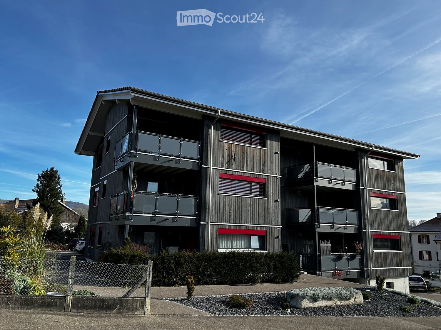 modern 3 story apartment building, black exterior, red window awnings, multiple balconies