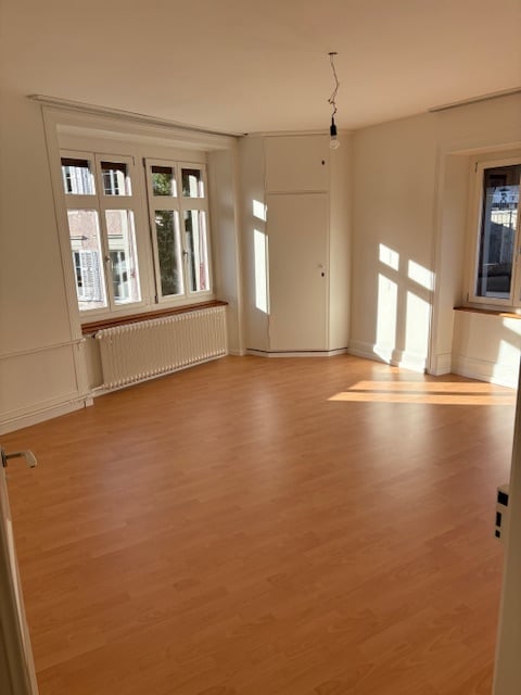 empty room, wooden floor, three windows, white walls, white radiator, hanging light