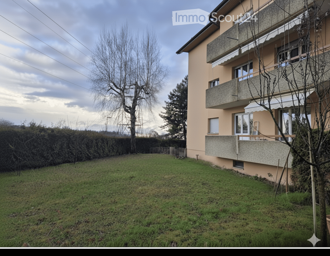 Exterior view of a two-story building with balconies, surrounded by a small, green lawn and greenery.