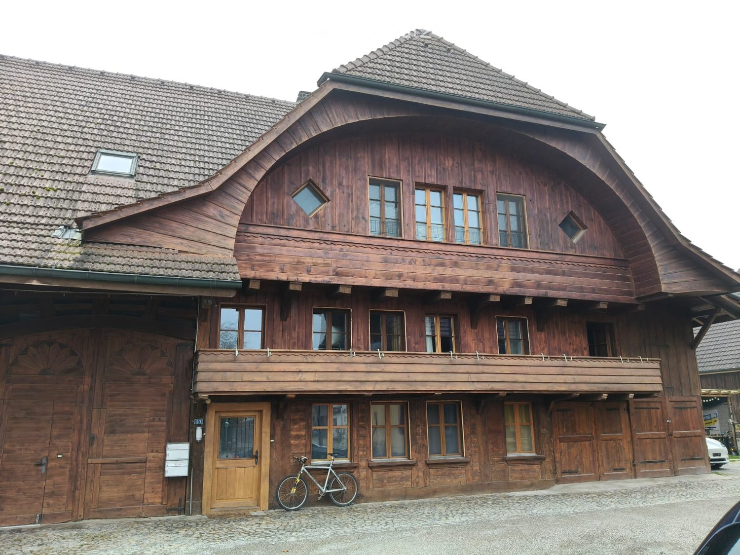 Wooden house, multiple large windows, wooden balcony, raised ground floor, large doors, bicycle