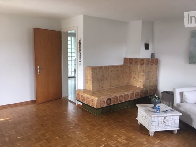 White sofa, tiled bench with fireplace, brown wooden door, white coffee table, potted flower, white walls