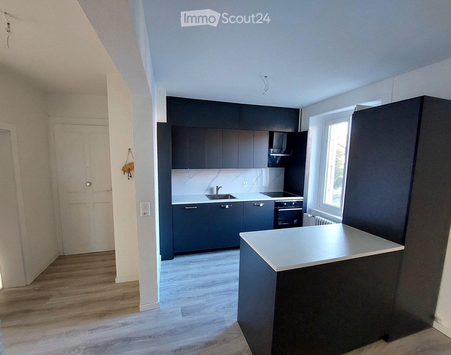 modern, minimalistic kitchen with black cabinets, white countertops, central island, gas stove, oven, dishwasher, sink, marble backsplash, wooden floor, white walls