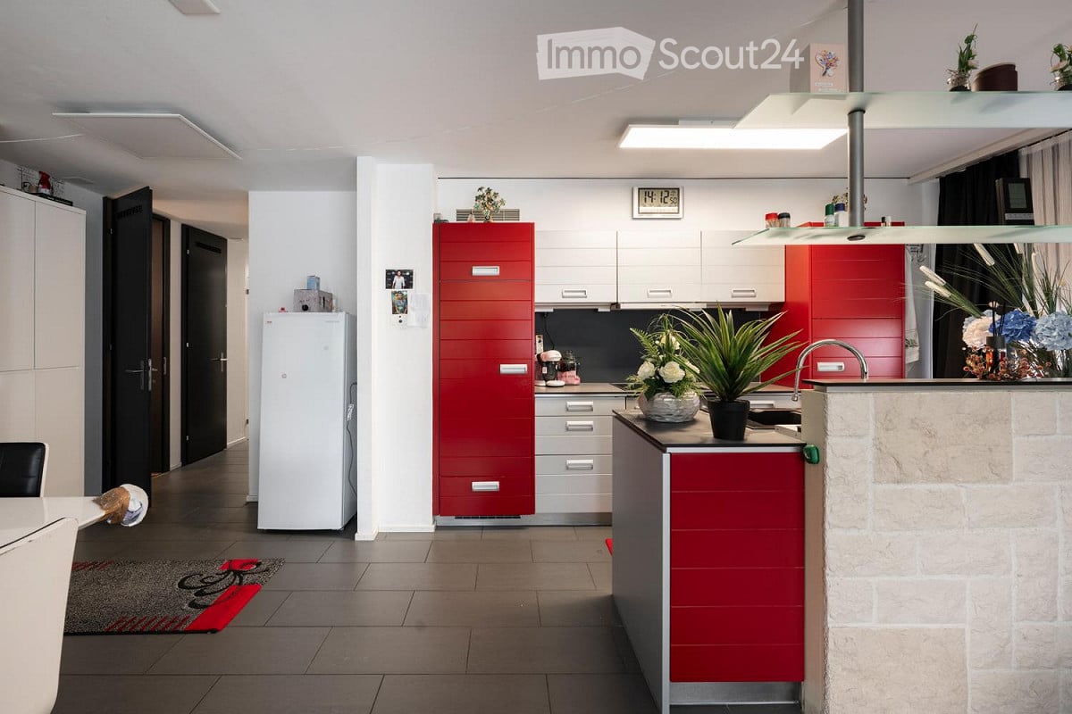 modern open-plan kitchen with sleek red cabinets and modern white appliances, marble counter-top, stainless steel sink, white shelves, and tiled floor