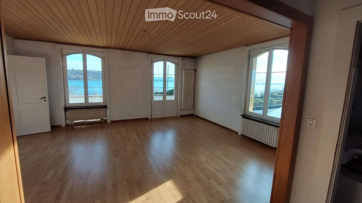 3 windows with view to sea, wooden floor, white walls, two radiators
