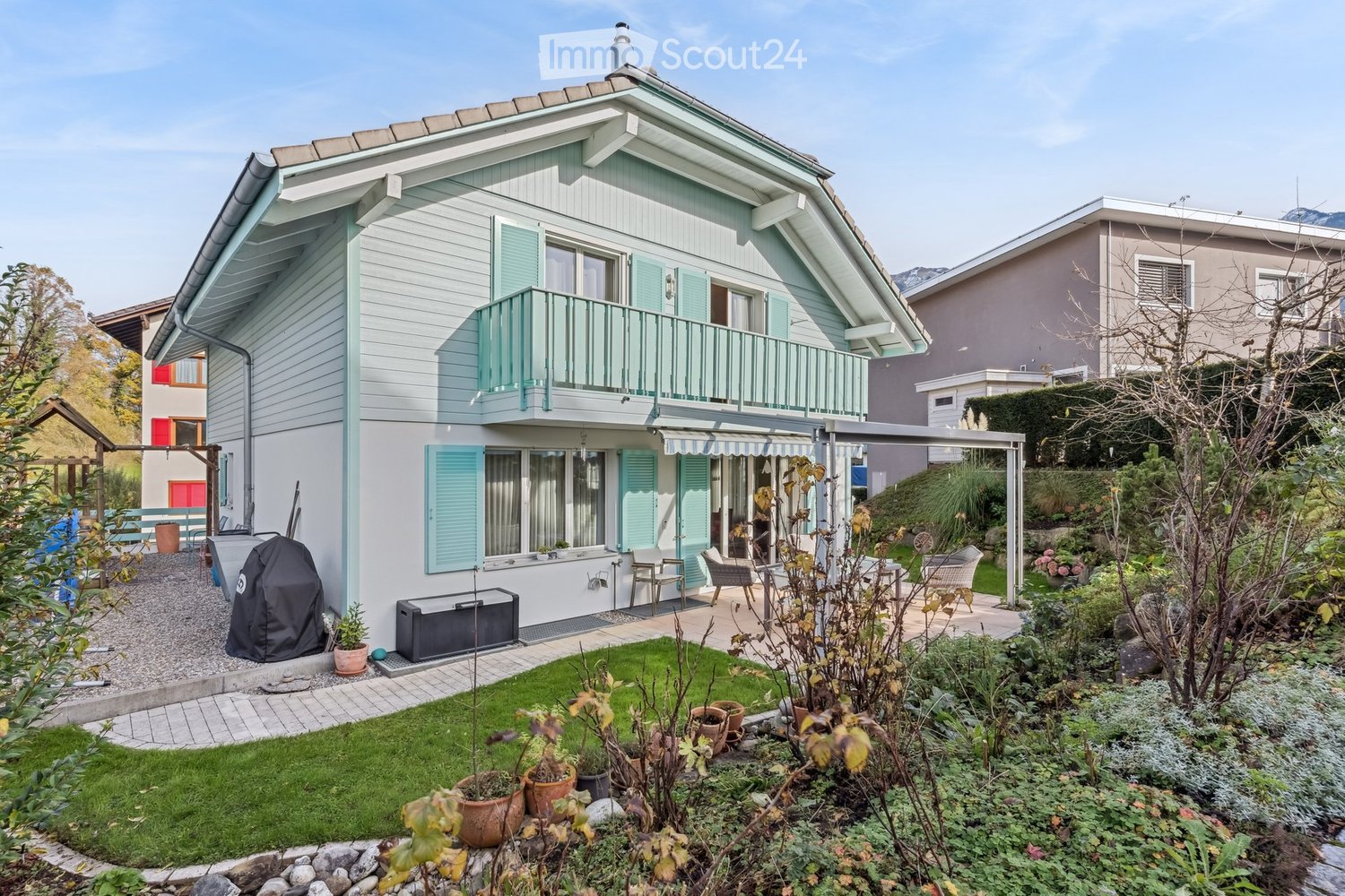 Two-story house, white exterior, green shutters, balcony, garden, patio, storage boxes, and plants.