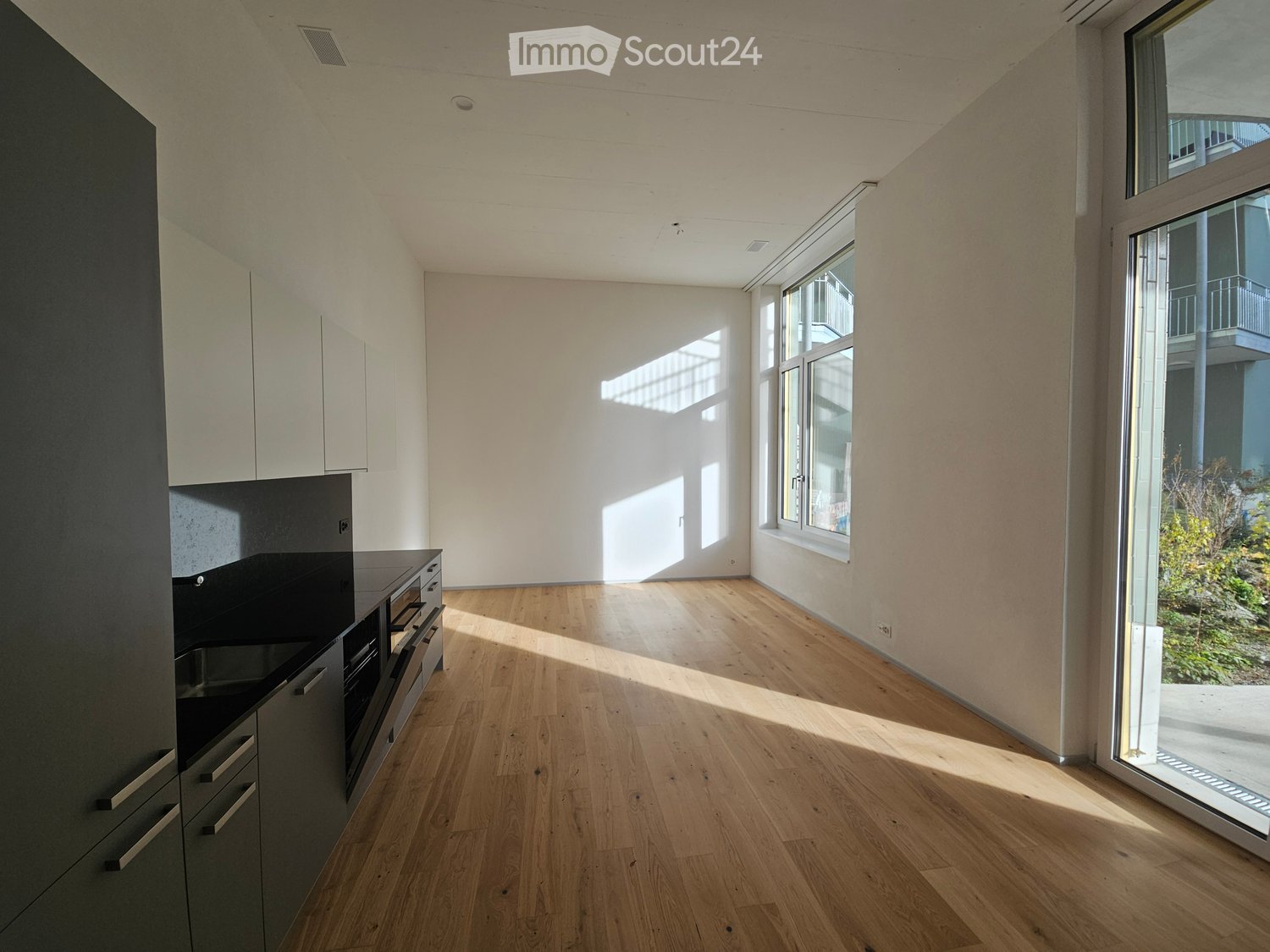 empty kitchen, wooden floor, white cabinets, black countertop, large window