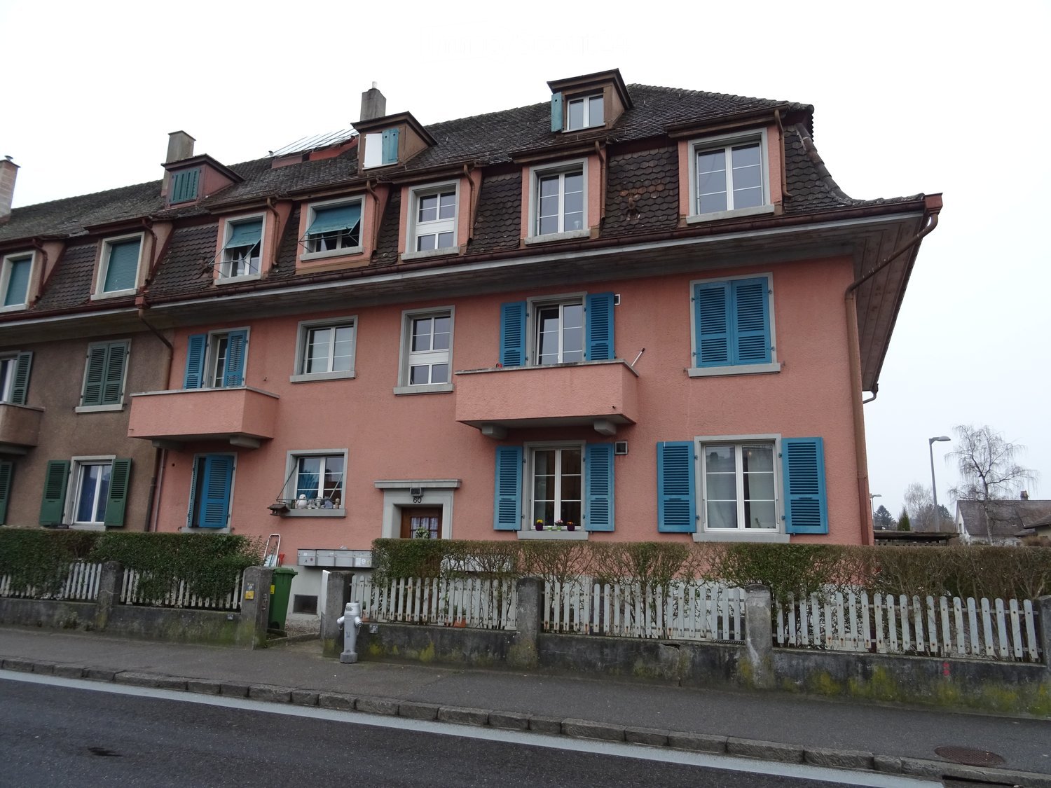 4 story building, pink paint, brown roof, blue shutters, large front yard, white fence