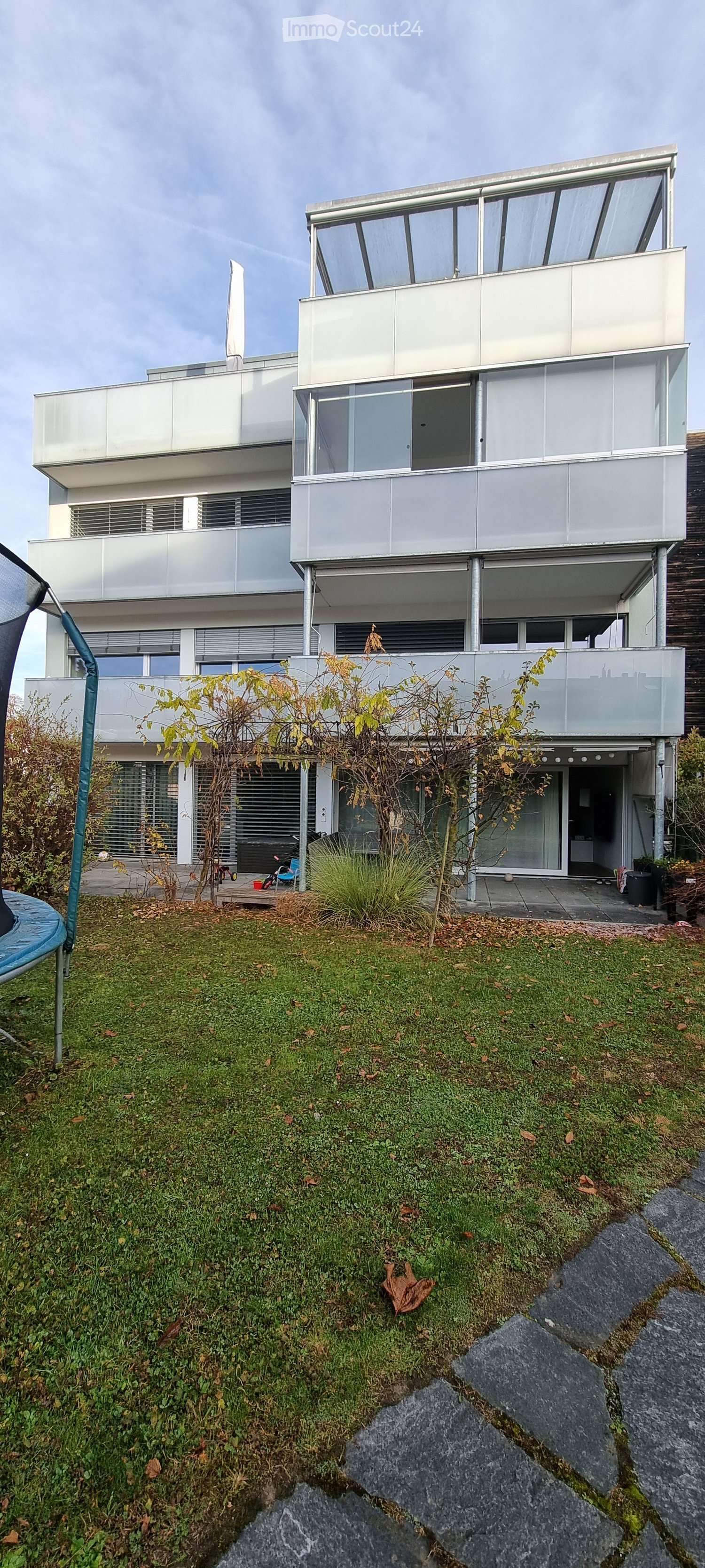 3 story house, gray building, windows, plants, wooden wall, grass, concrete pavement