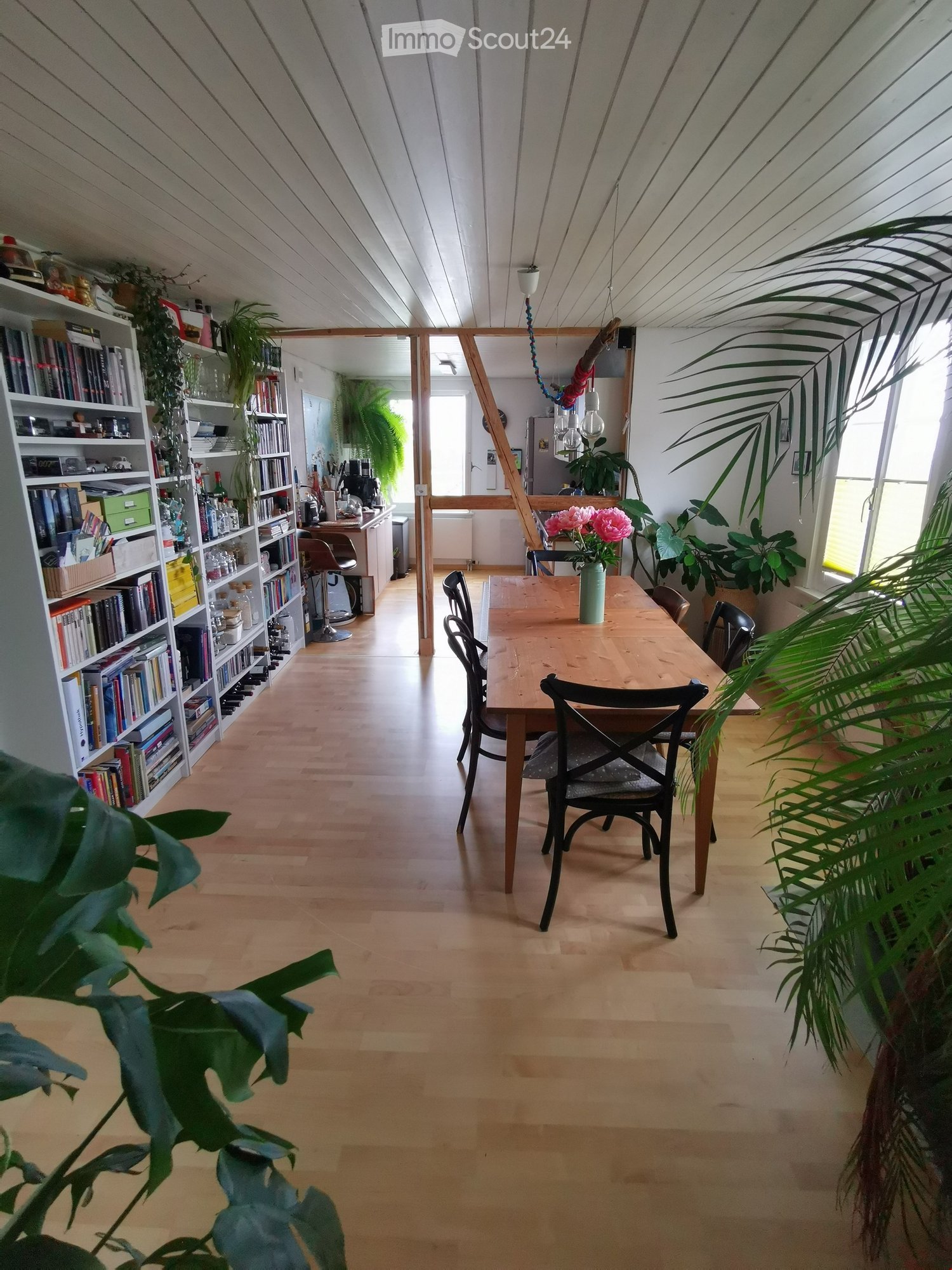 dining room, wooden floor, wooden table, chairs, shelf with books, plants, flowers in vase