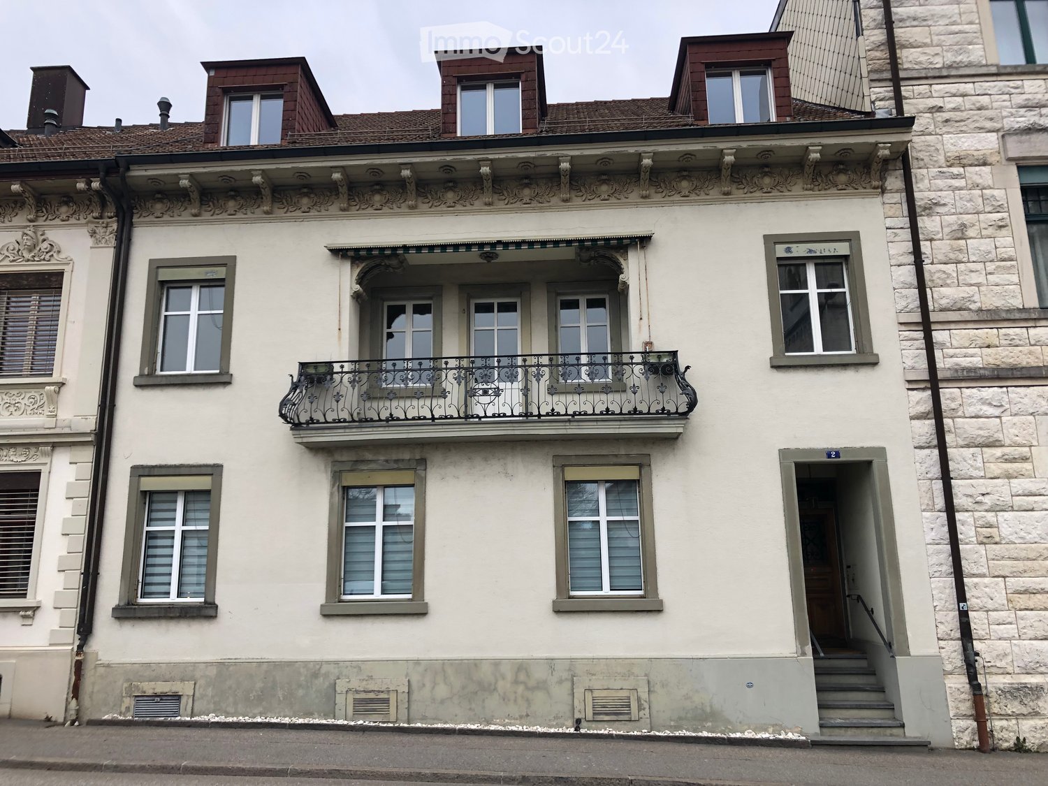 A multi-story building with a decorative facade, featuring ornate balconies, arched windows, and a stone exterior. The building appears to be a historic or traditional architectural style.