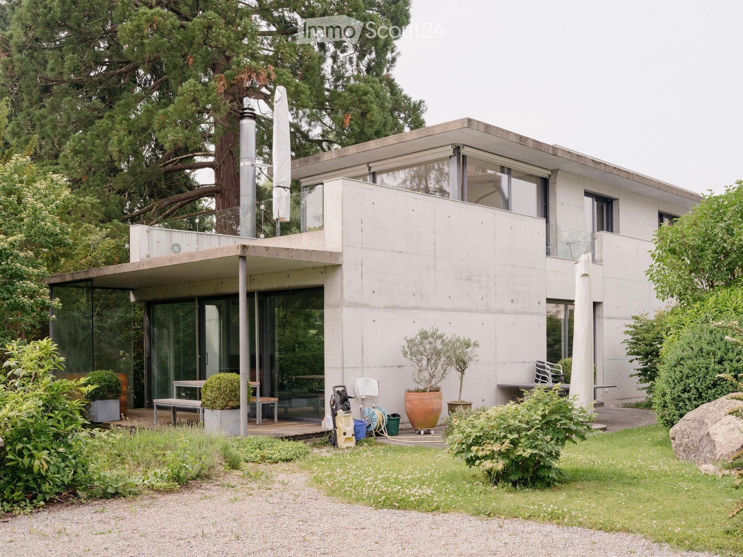 two-story modern concrete house, large glass windows, front terrace, wooden bench, front yard