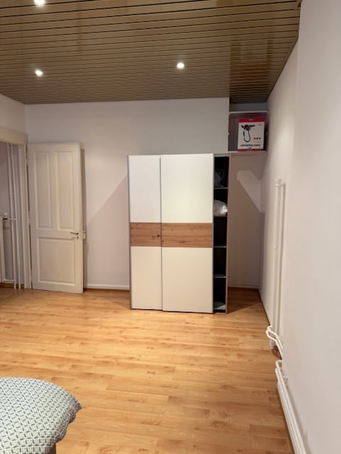 A room with a double bed, a white door, a white and wooden wardrobe, a wooden floor, and a white wall.