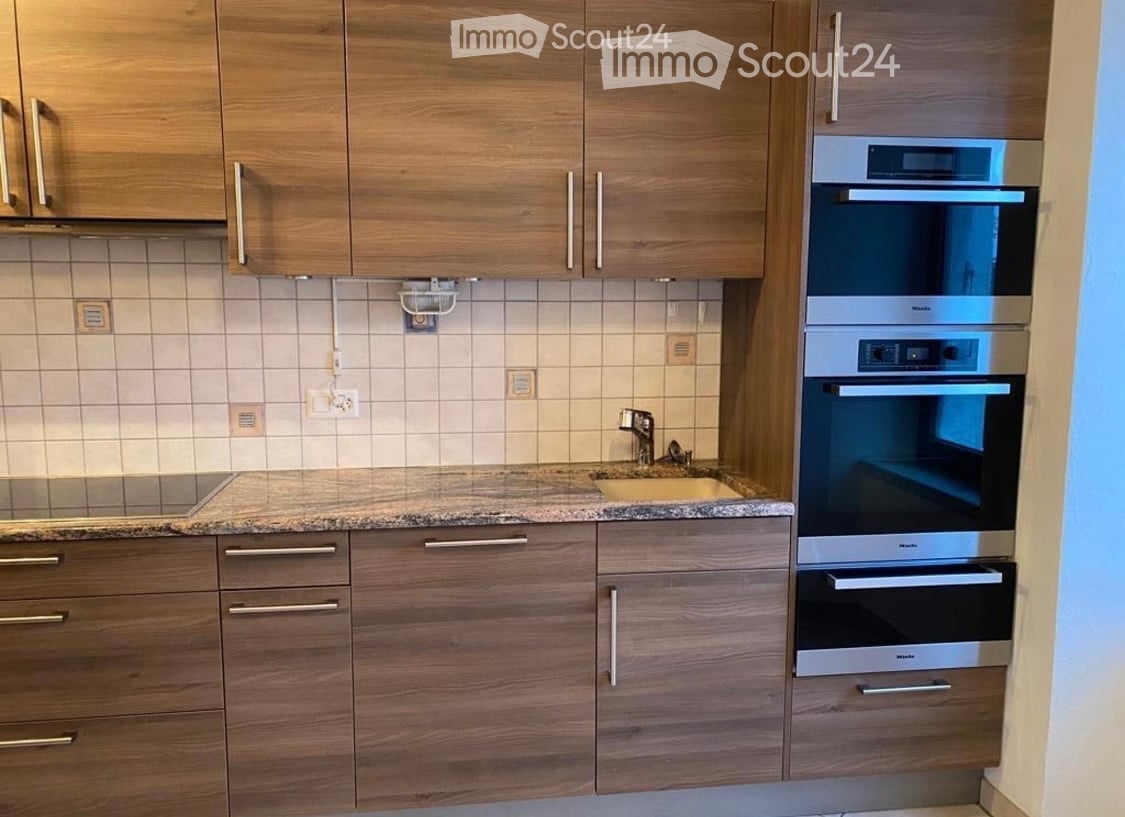 The kitchen features a gas stove, a sink, and two ovens integrated into wooden cabinetry with a granite countertop. There is an electric outlet mounted on the wall.