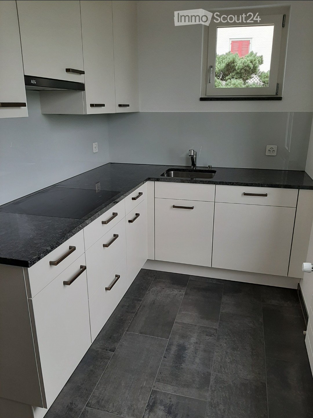 Modern kitchen with granite countertops, stainless steel sink, white cabinets, gas hob, electrical outlets, and a window with shutters