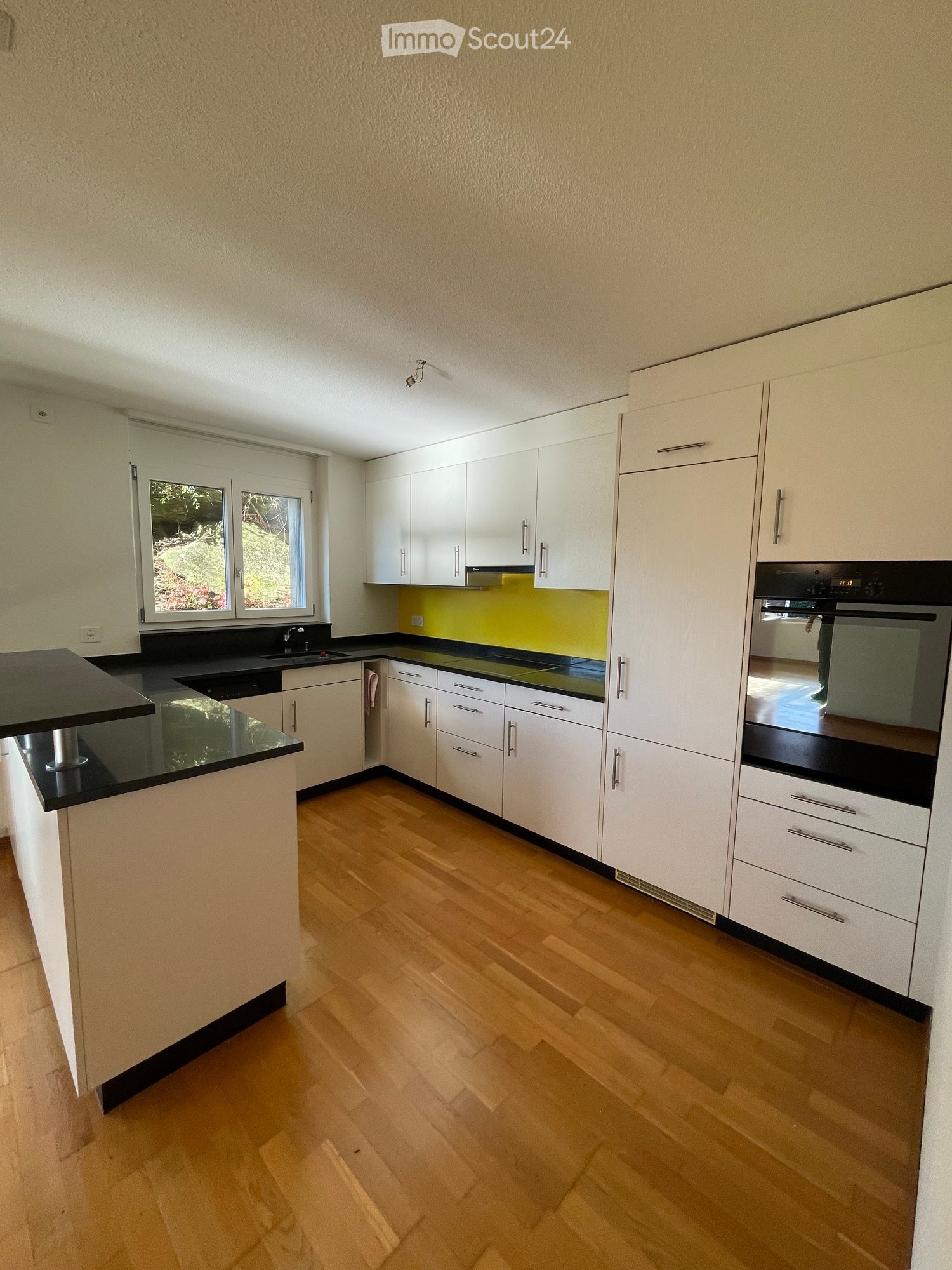 A kitchen with white cabinets, black countertops, a yellow wall, wooden floors, and modern appliances.