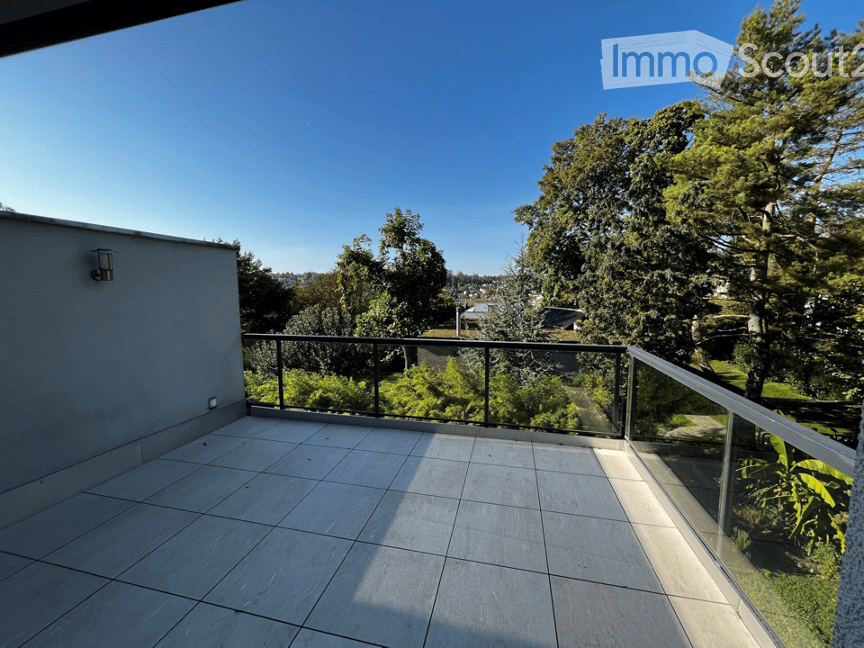 Balcony with tiled floor, glass railings, surrounded by greenery