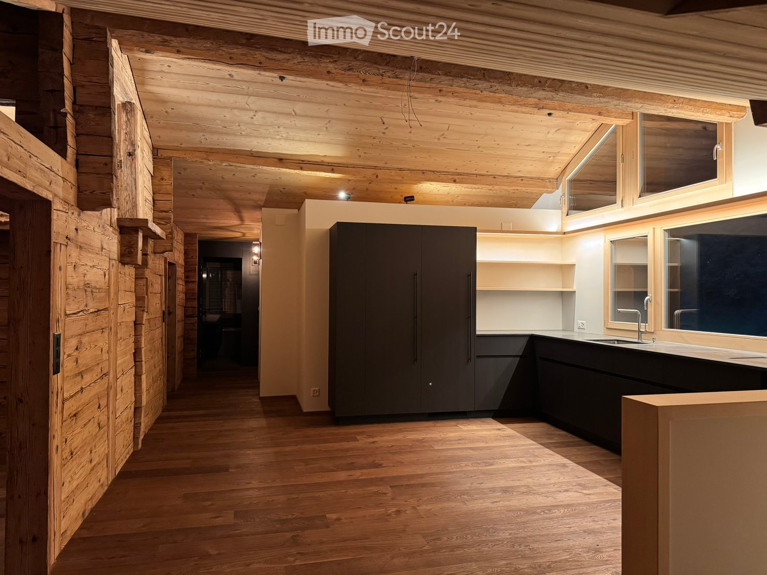 wooden interior, wooden floor, modern kitchen with black cabinets and countertops, large windows, large sink with faucet, wall-mounted lighting