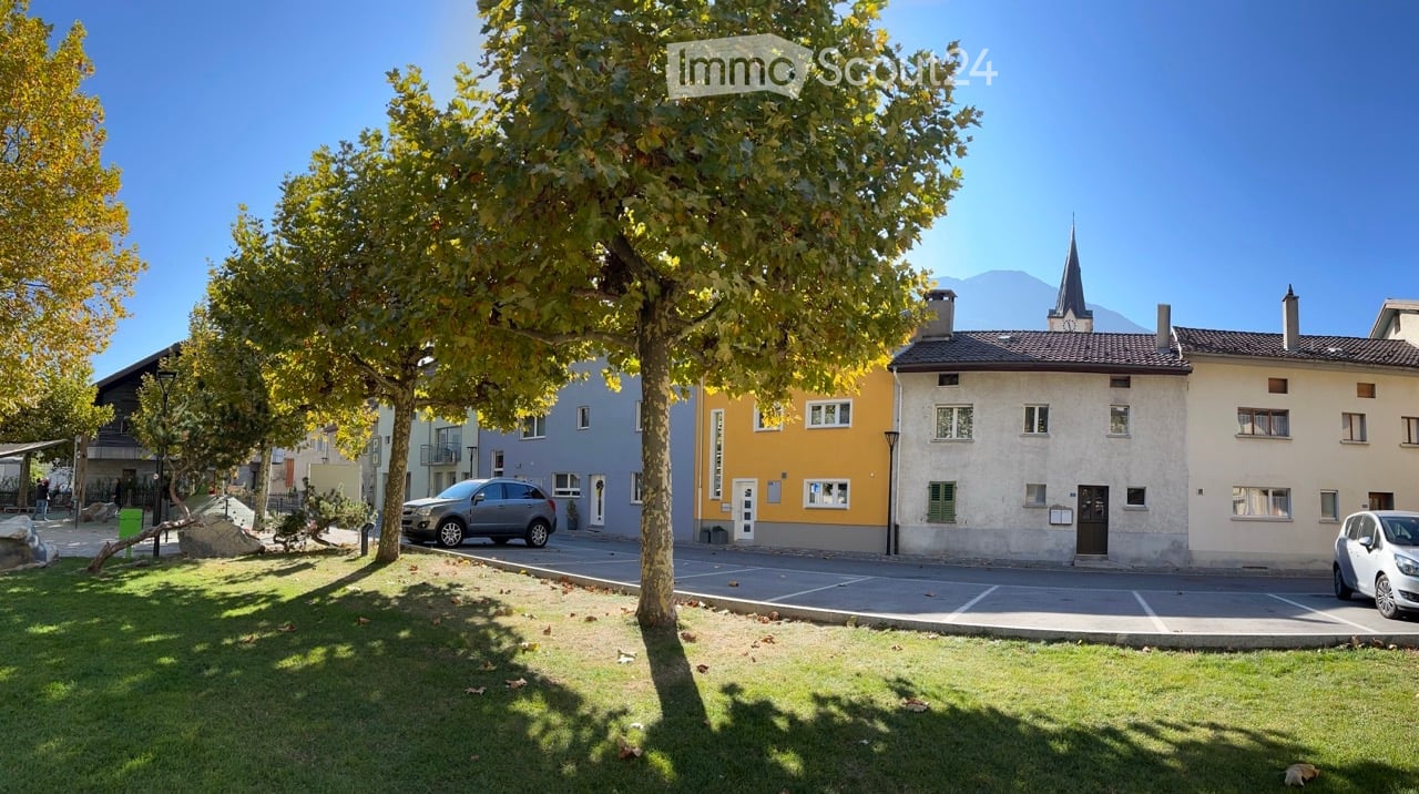 Row of houses, cars parked in front, green trees, grassy area, street with marking