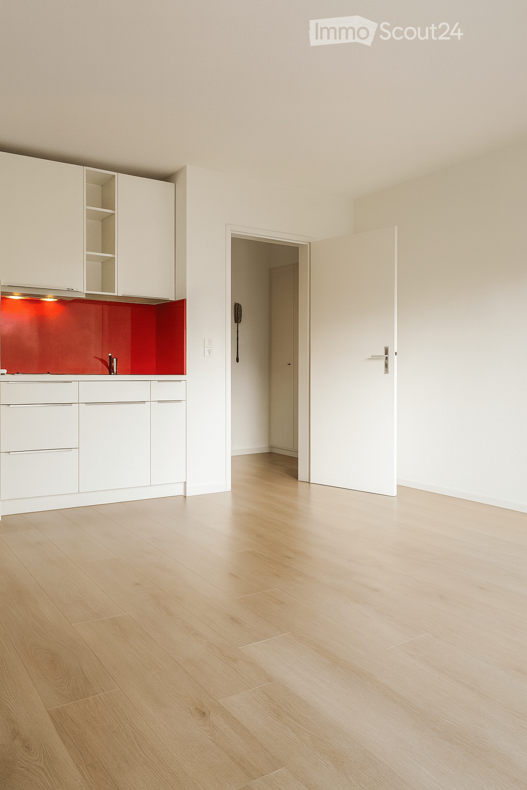 Modern kitchen, white cabinets, red backsplash, wooden floor, open to hallway