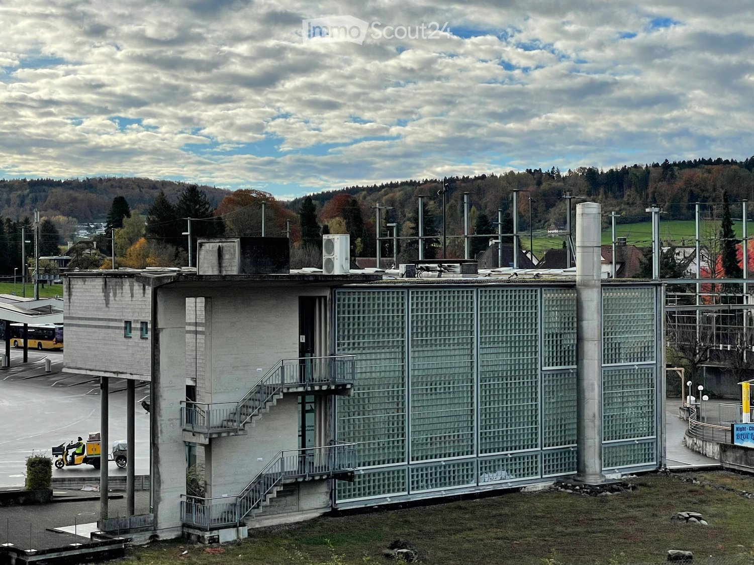 Single story building, glass windows, exterior staircase, air conditioning unit, large parking area, electrical transmission lines