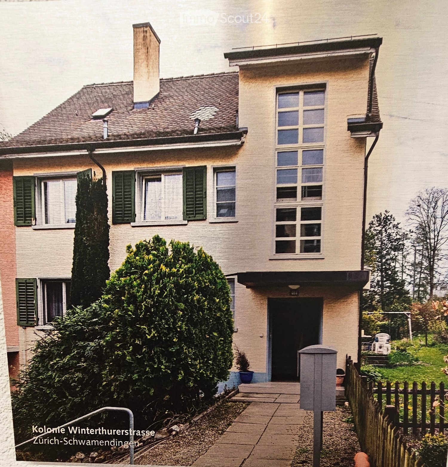 Raised ground floor, Two story house, brown roof, multiple windows, brick wall, pathway, wooden fence, mailbox