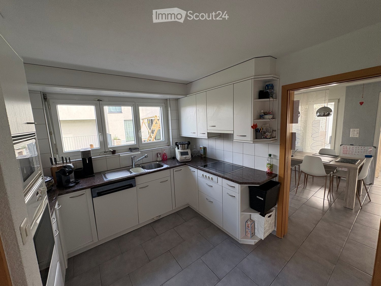 Modern kitchen with white cabinetry, tiled floor, granite countertops, built-in oven, dishwasher, and modern appliances.