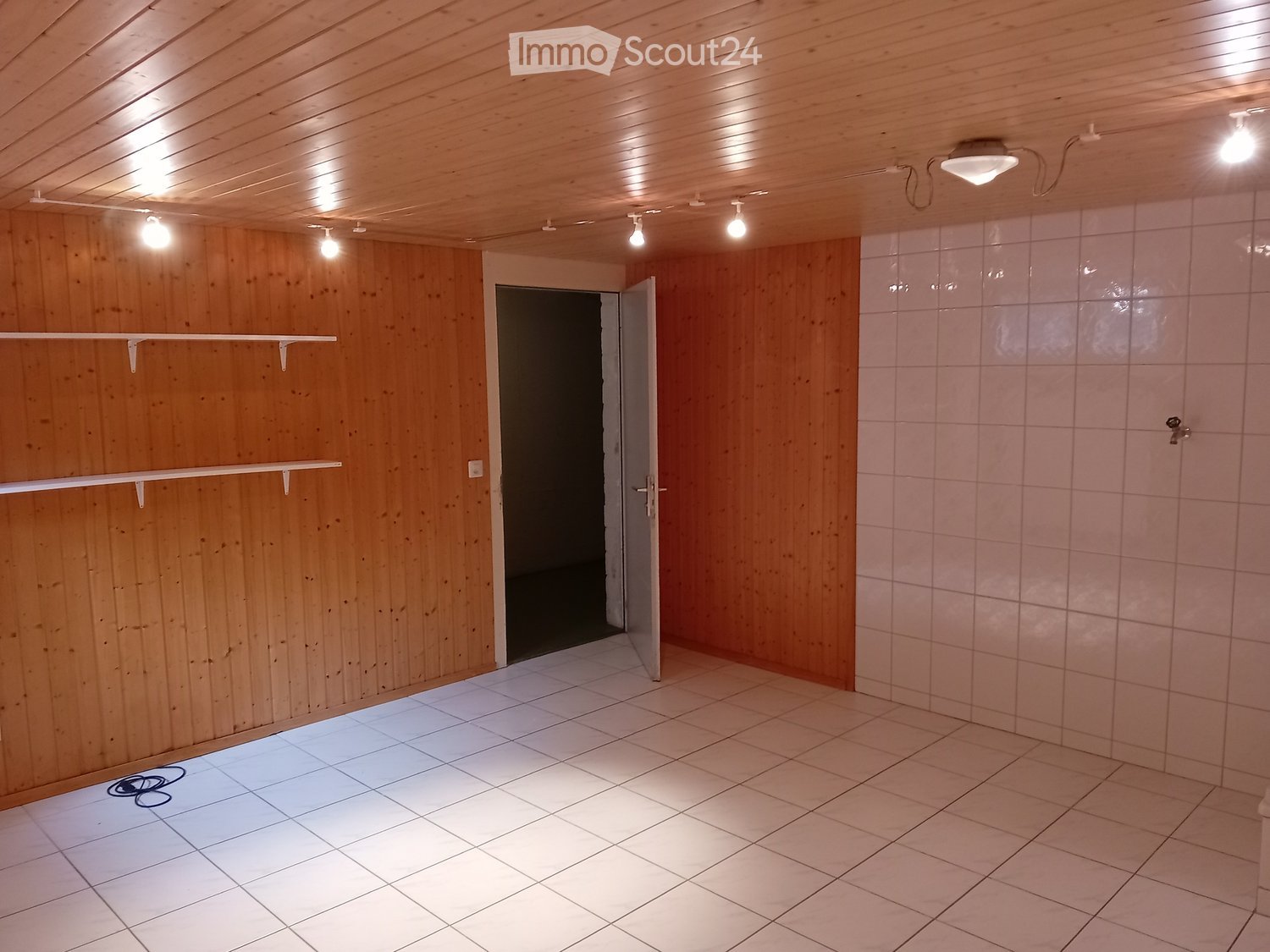 Empty room with wooden walls, white tile floor, mounted shelves, and lights