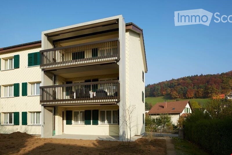 two-story building, green shutters, white walls, balconies, fenced garden, autumnal hills
