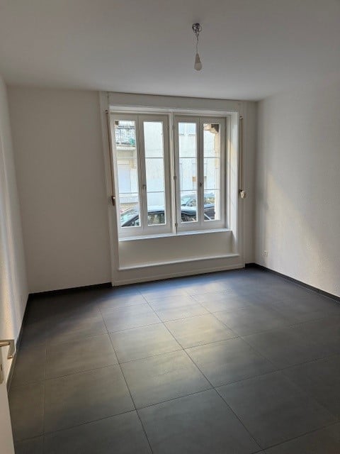 Empty room with white walls, tiled floor, large window, hanging light