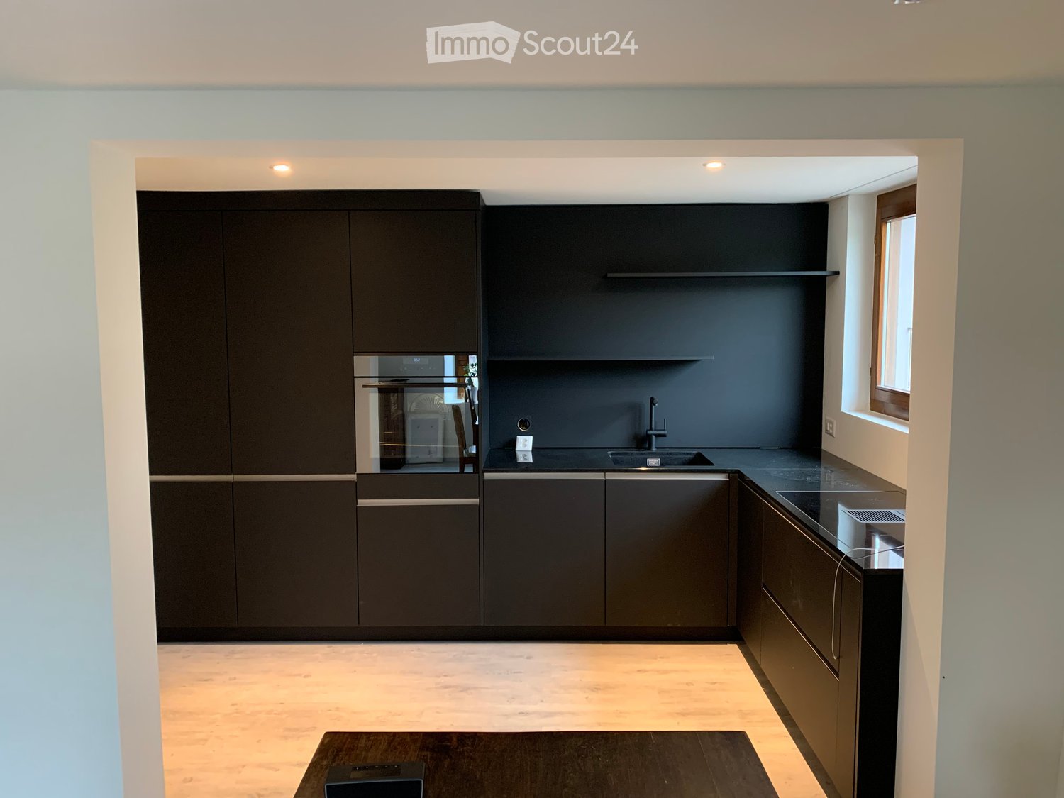 Modern kitchen with black walls, wooden floor, kitchen island, built-in appliances, white window