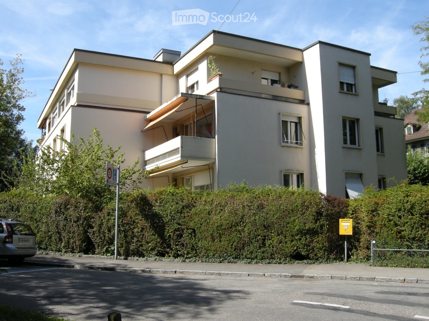 3 story apartment, beige walls, green windows, beige balcony, garden in front