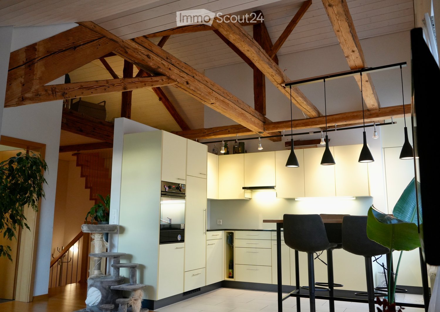 high ceilings, exposed wooden beams, modern white cabinetry, built-in oven and microwave, counter-top for bar stools, pendant lights, open layout