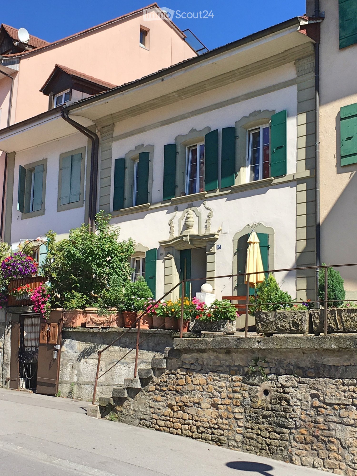 3 story stone house, pink color, brown windows, green shutters, brown door, staircase, plants