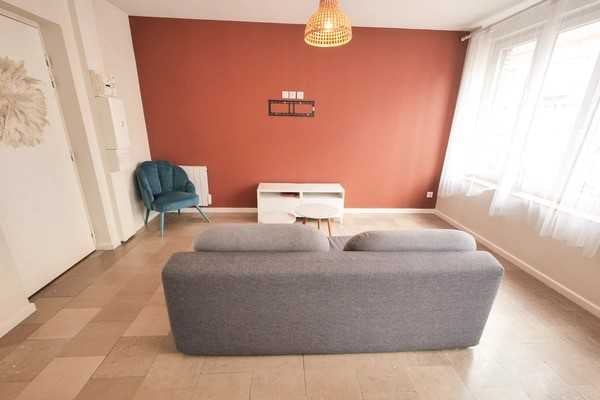Modern living room with wooden floor, gray couch, red wall, blue chair, white shelf, central light fixture