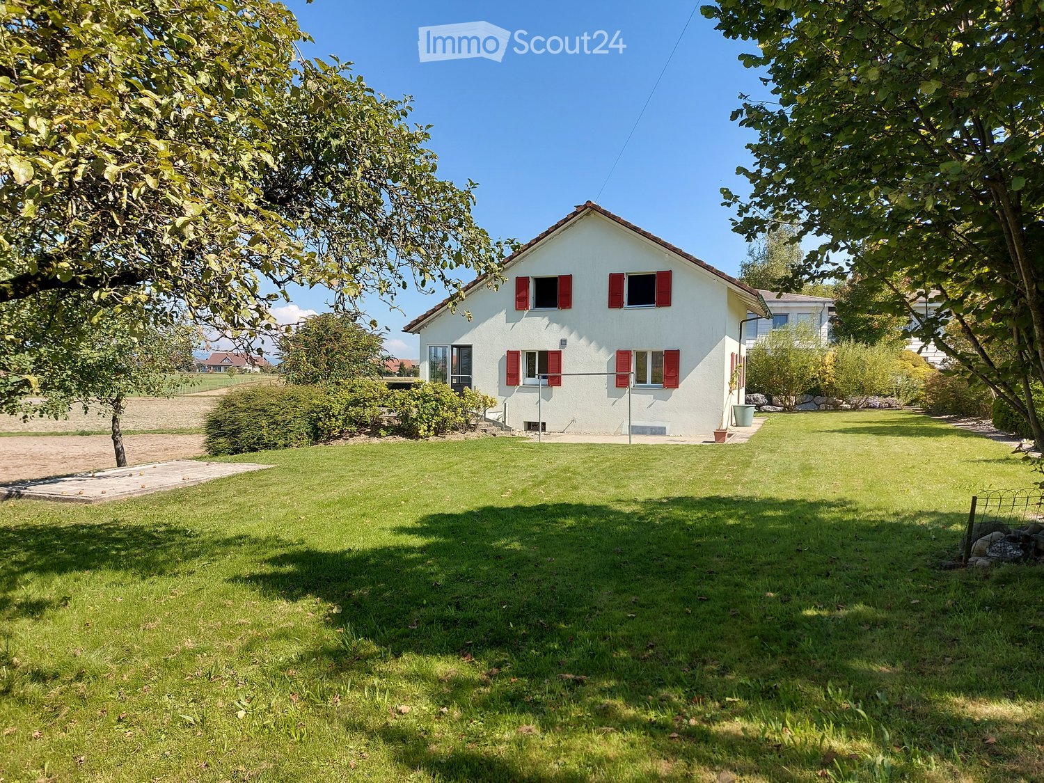 white house, red shutters, two-story, brick roof, green lawn, small garden, trees