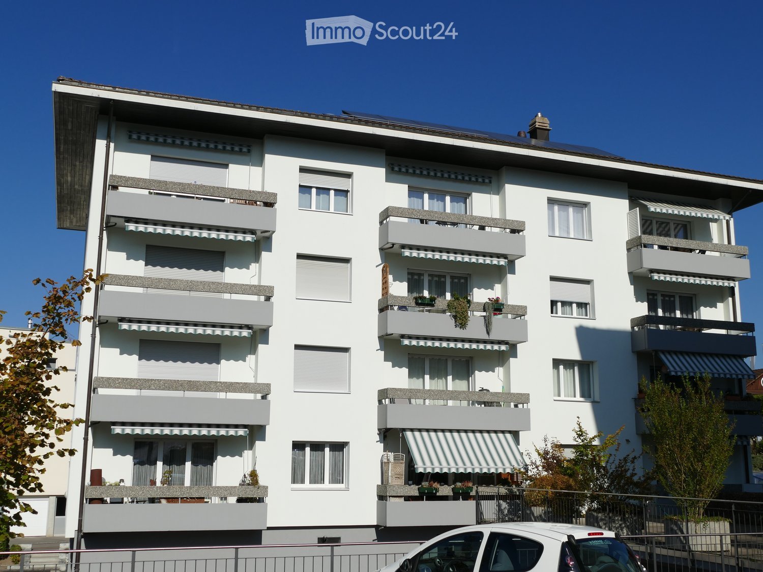 Apartment building, white exterior, multiple balconies, solar panels on the roof
