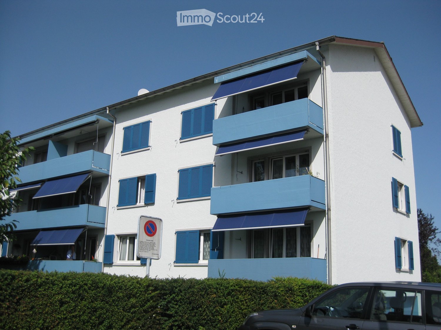 white building, 4 floors, blue balconies, blue shutters, awnings