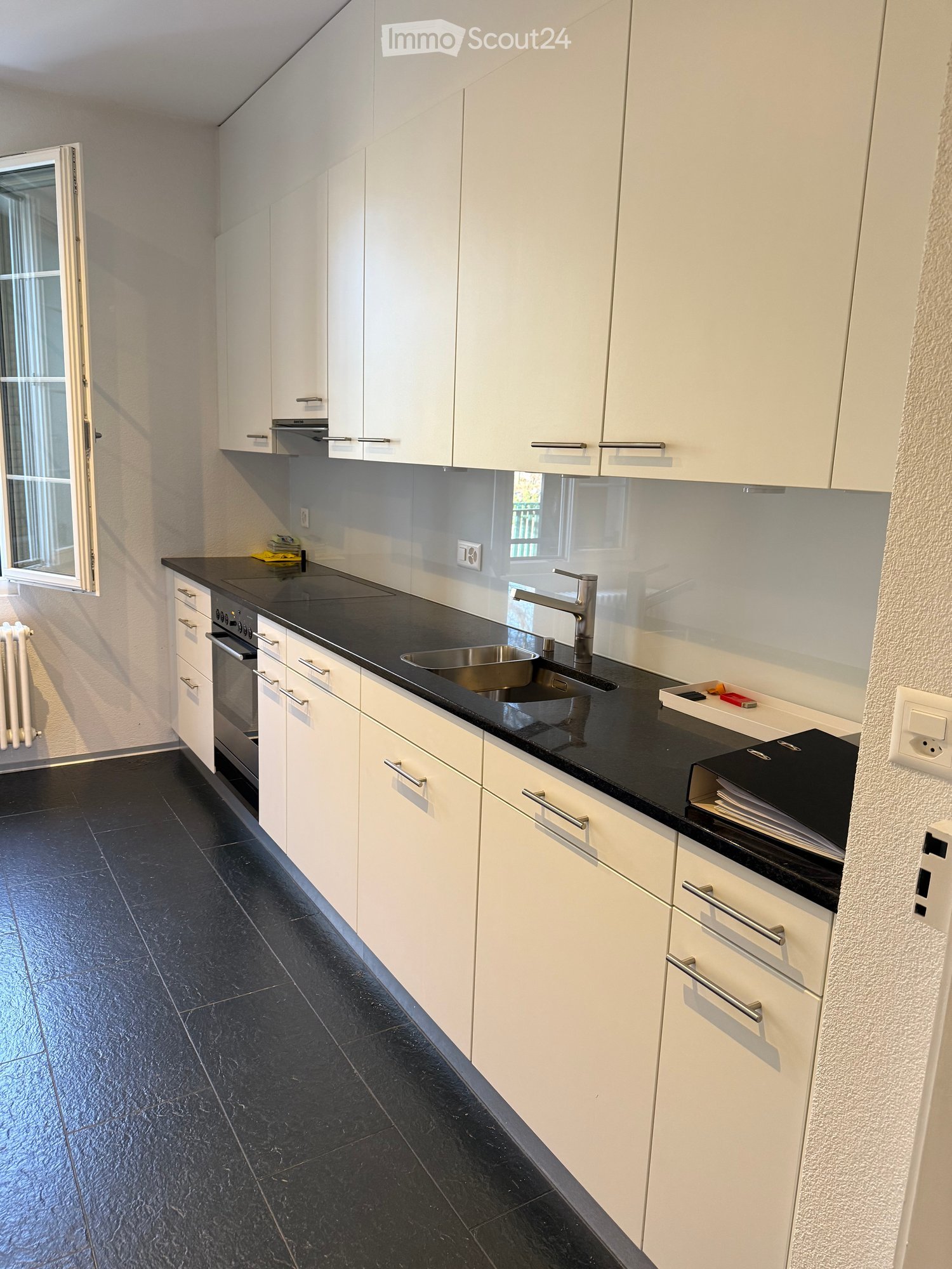 modern kitchen, black counter, white cabinets, stainless steel sink, dishwasher, washing machine, window, radiator