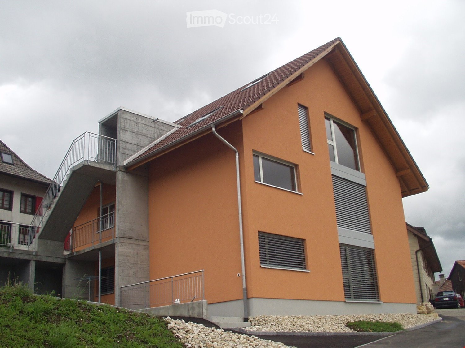 2-story residential building with orange exterior walls, tiled roof, and balconies. The building has large windows and a modern architectural design.