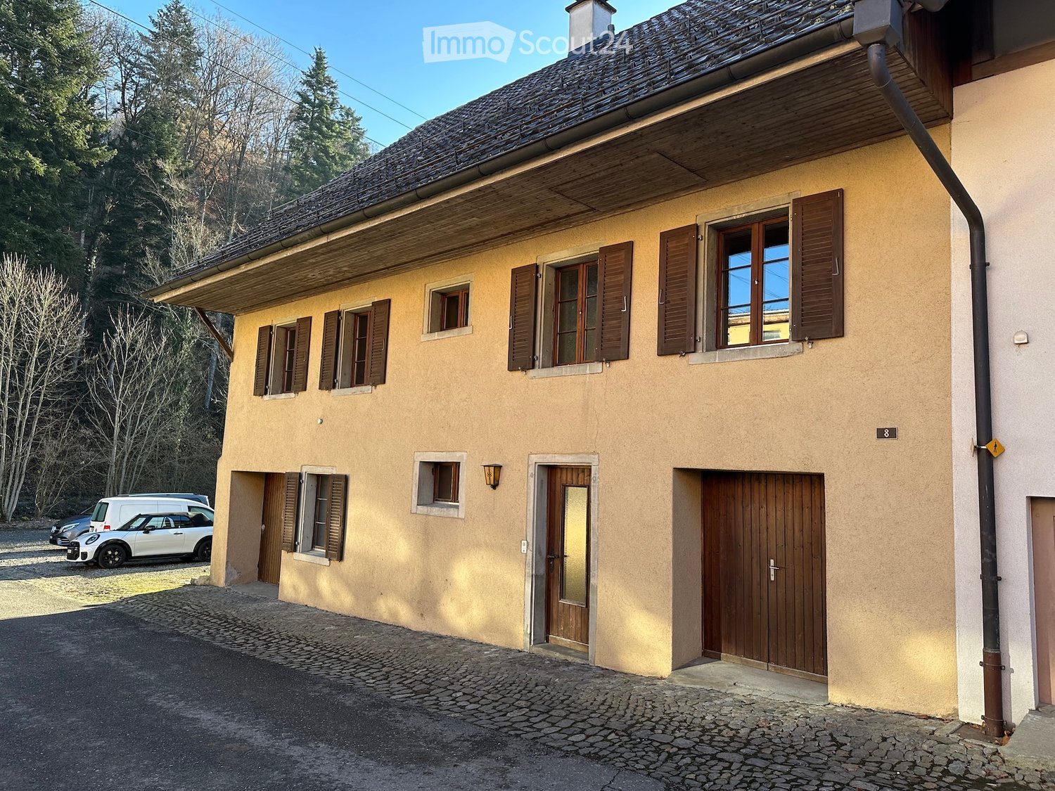 2-story yellow house with wooden shutters, black roof, brown wooden doors, cars parked in front